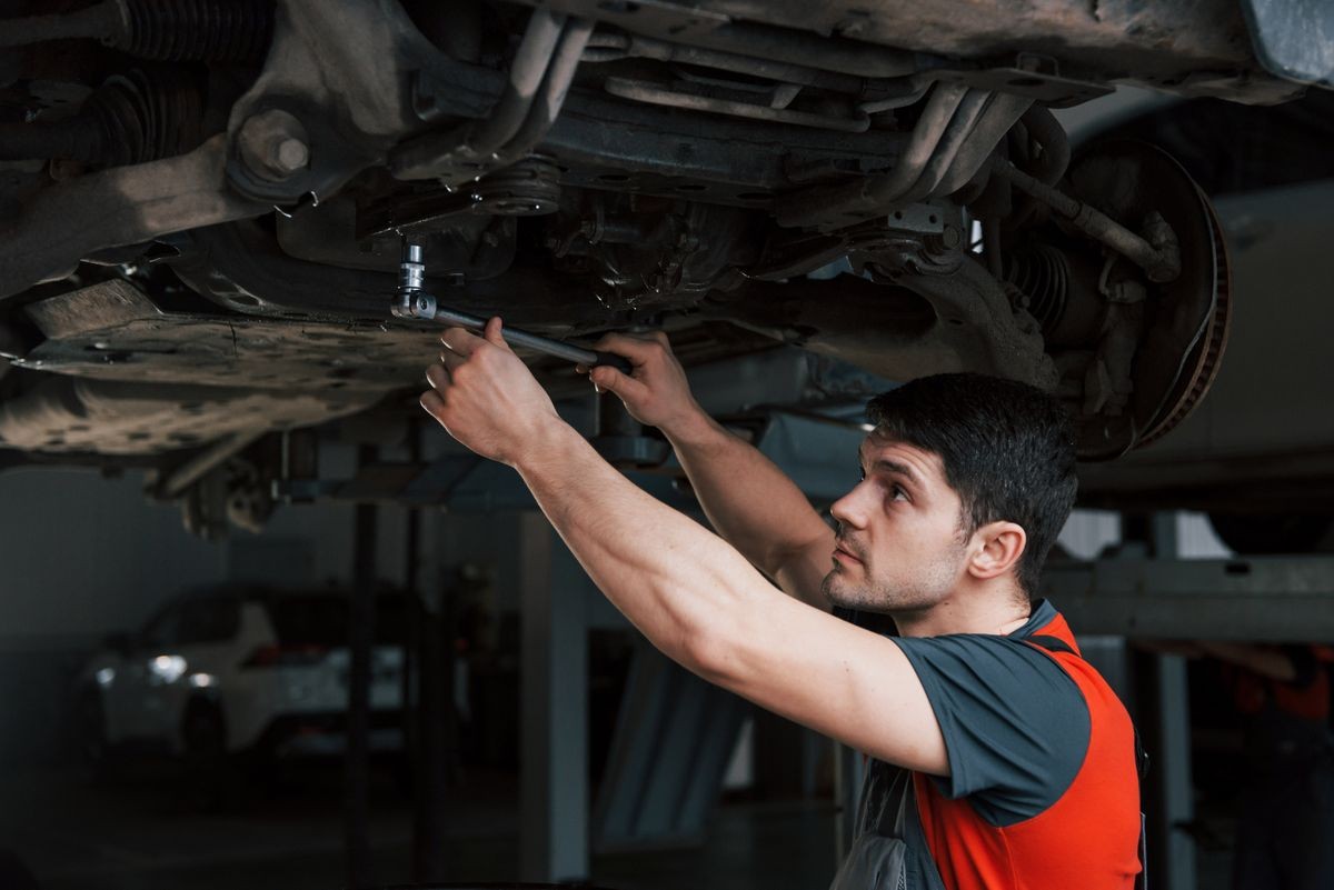 Need a solid hand. Man at the workshop in uniform fixes broken parts of the modern car.